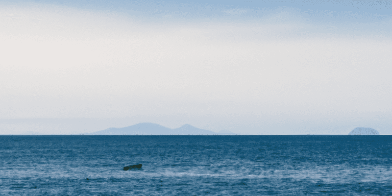 A small boat sailing on a vast ocean, with a distant island in the horizon.